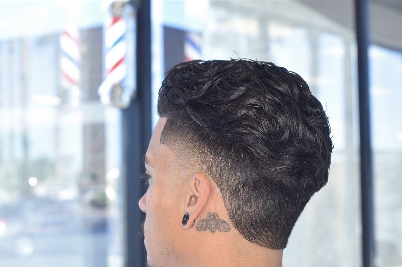 Back view of a men's wavy tapered haircut with barber poles in window
